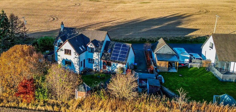 Aerial view of rural farmhouse with blue roof, solar panels, outbuildings and surrounding fields