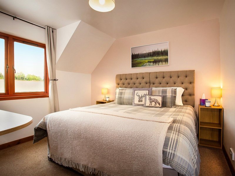 Bright attic bedroom with double bed, upholstered headboard, wooden nightstands and window with countryside view