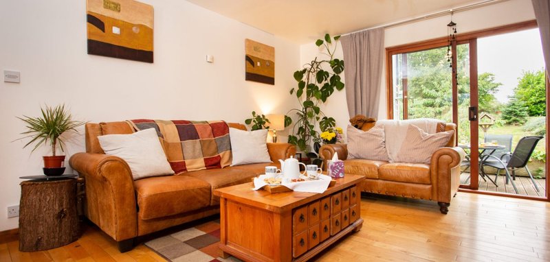 Bright living room with orange leather sofas, wooden coffee table, and patio doors to garden