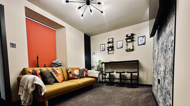 Modern living room with mustard-yellow sofa, orange accent wall, fireplace, and contemporary ceiling light