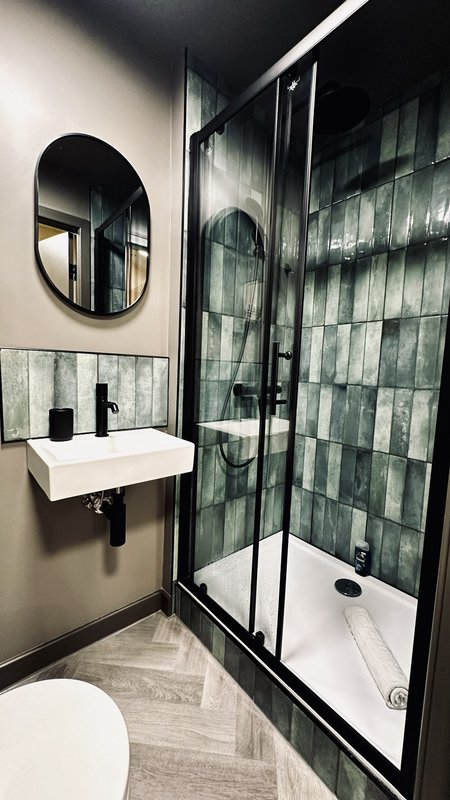 Modern bathroom with walk-in shower, white sink, oval mirror and green tile walls