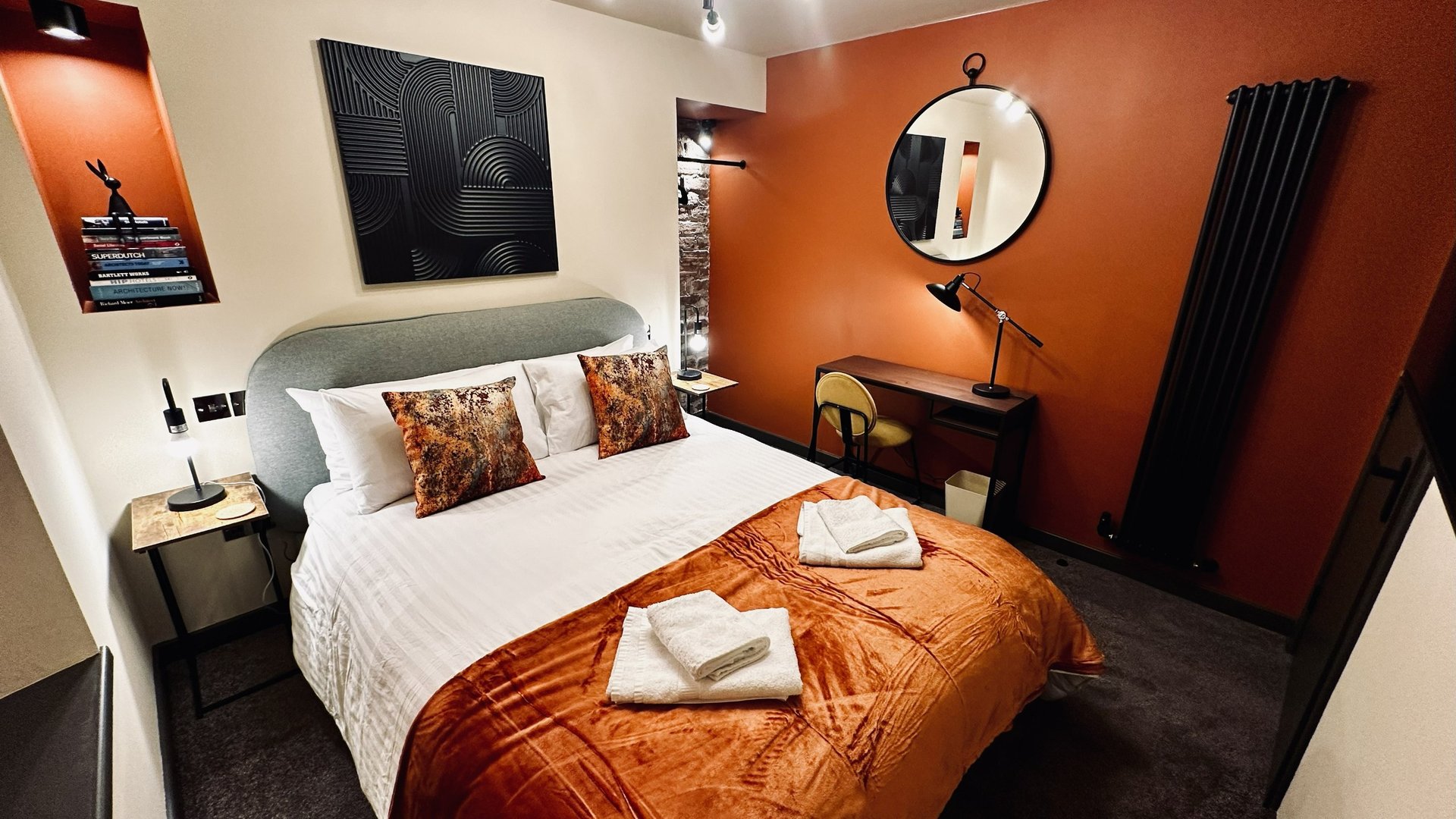 Modern bedroom with double bed, orange accent wall, round mirror and contemporary furnishings