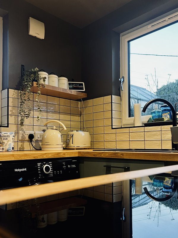Modern kitchen with yellow tile backsplash, wooden countertop, black appliances and window view