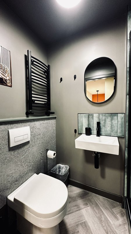 Modern bathroom with toilet, wall-mounted sink, round mirror and grey tile walls