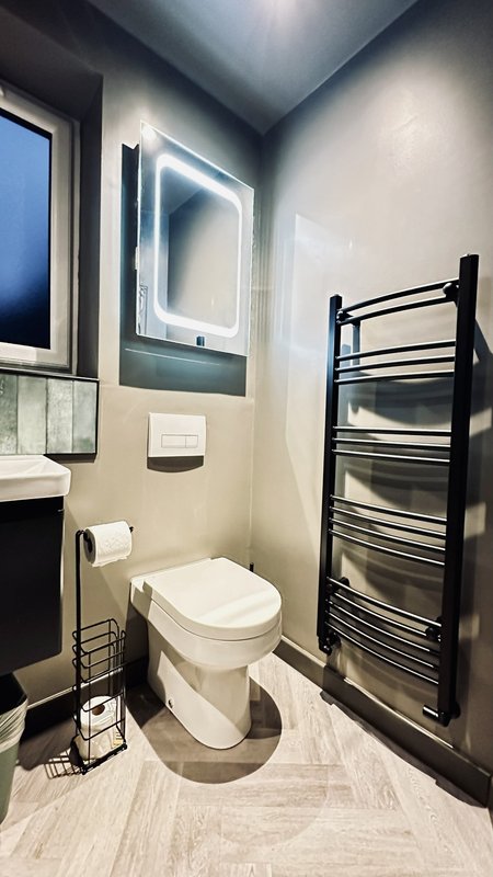 Modern bathroom with toilet, heated towel rail, illuminated mirror and window