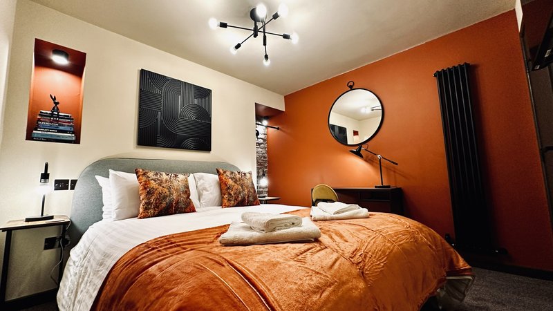 Modern bedroom with orange accent wall, double bed with orange bedding, round mirror and ceiling light fixture