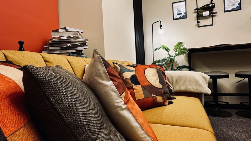 Modern living room with yellow sofa, colorful cushions, orange accent wall, and framed artwork
