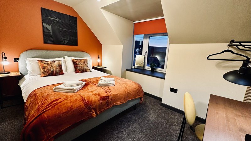 Modern bedroom with orange accent wall, double bed, bedside lamps and window