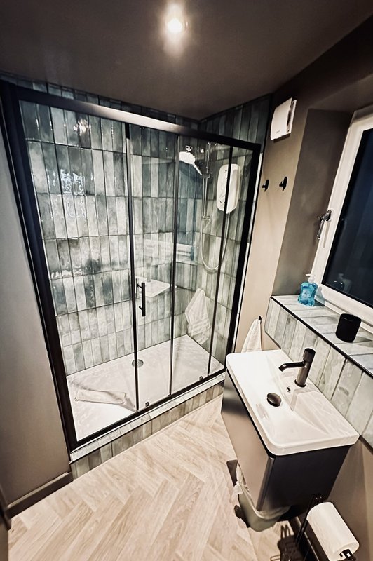 Modern bathroom with black-framed shower enclosure, white sink, toilet, and light wood flooring