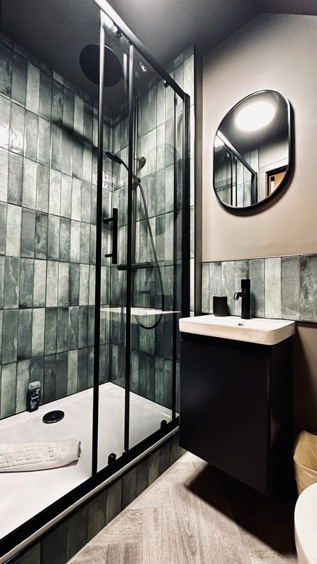 Modern bathroom with walk-in shower, black vanity, white sink and round mirror