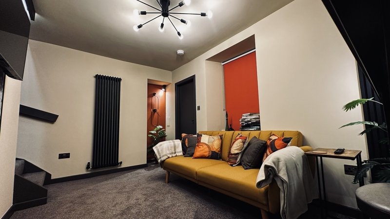 Modern living room with gold sofa, black radiator, orange accent wall and ceiling light