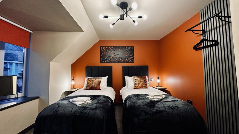 Modern bedroom with two single beds, orange accent wall, black bedding and decorative pillows