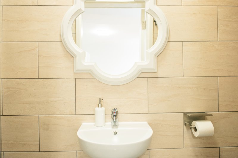 Bathroom with cream wall tiles, white pedestal sink, ornate mirror and toilet paper holder