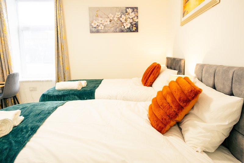 Bedroom with two beds, white bedding, orange and teal cushions, wall art