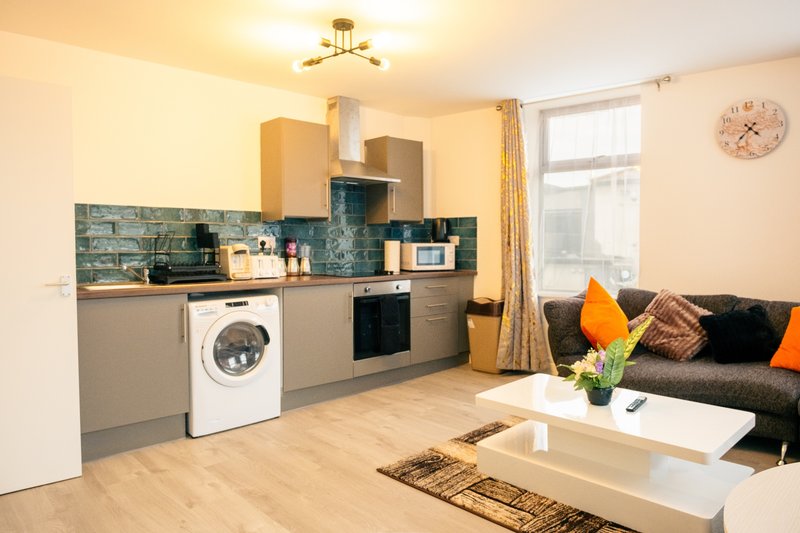 Open-plan kitchen and living area with grey cabinetry, washing machine, black sofa with orange cushions