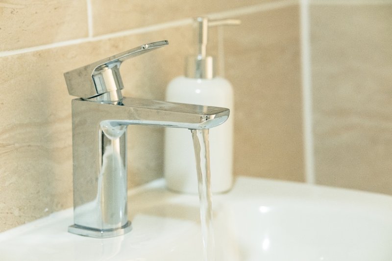 Modern bathroom sink with chrome faucet, white soap dispenser, and neutral tile wall