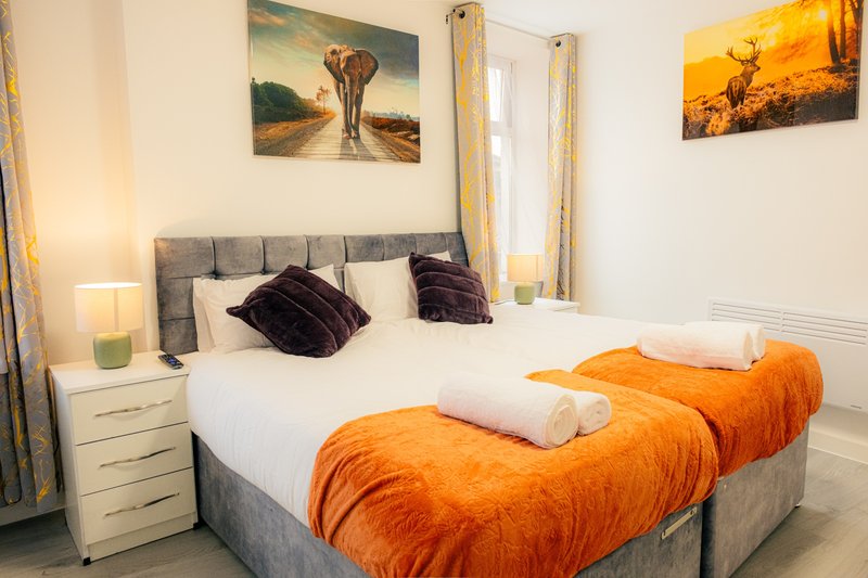 Bedroom with double bed, orange bedding, dark pillows, white towels, and framed wall art