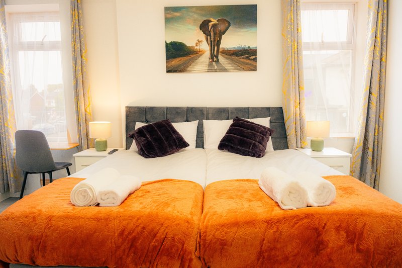 Bedroom with double bed, orange throw, black headboard and elephant artwork on wall