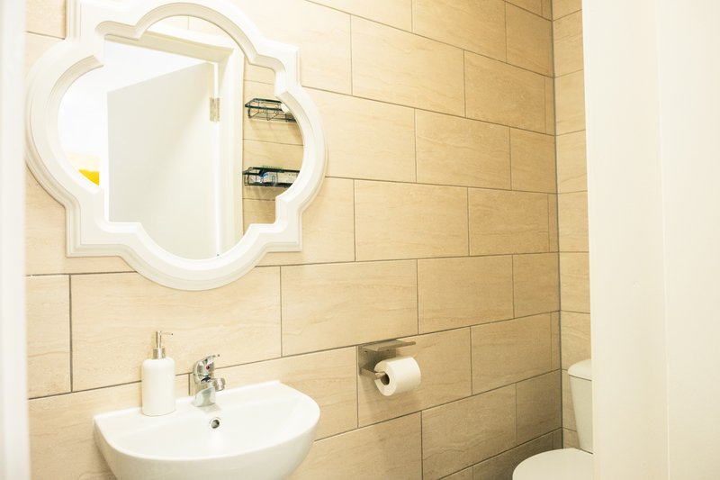 Bathroom with beige tiled walls, white sink, decorative mirror, and toilet paper holder