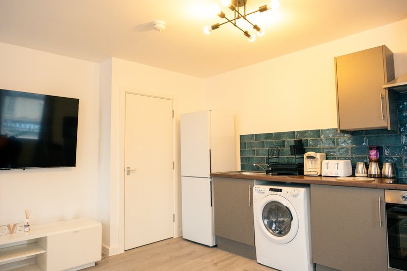 Modern kitchen with white appliances, teal tile backsplash, wall-mounted TV and wooden countertops