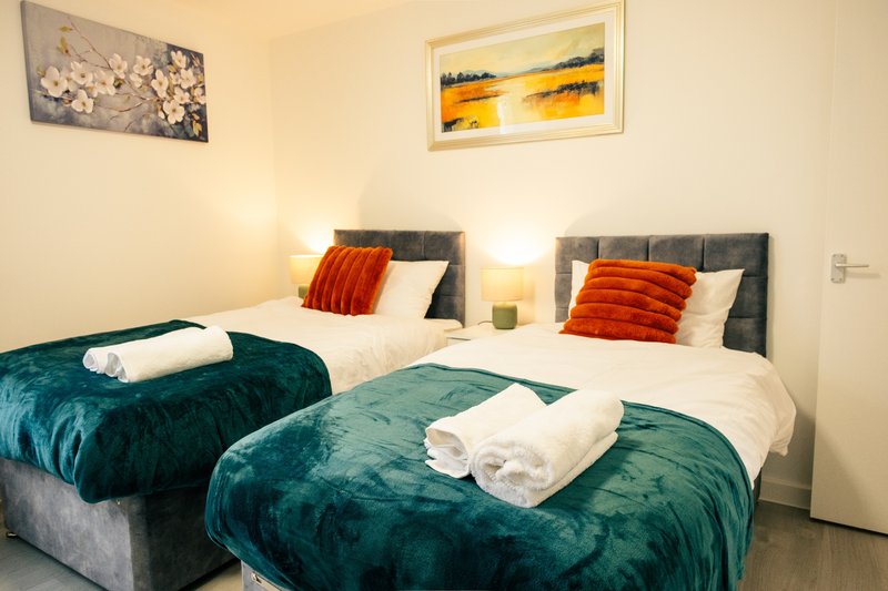 Twin bedroom with teal velvet bedspreads, white pillows, orange cushions and framed wall art
