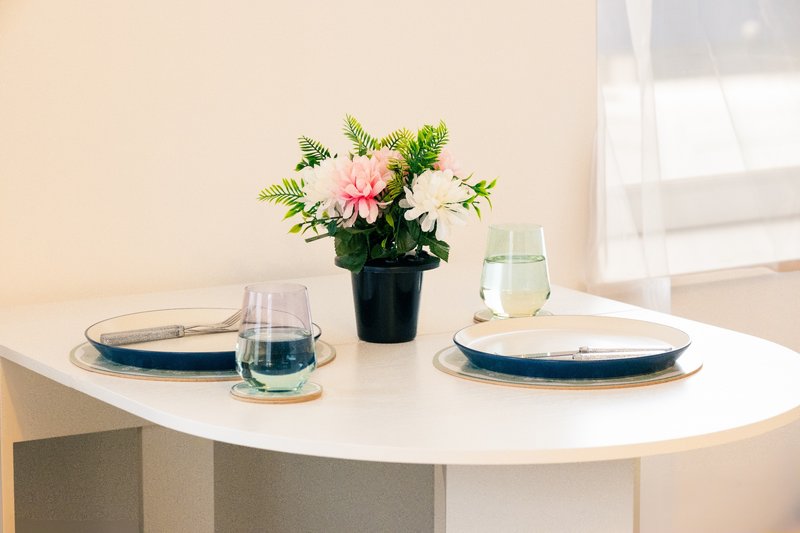 Modern round white dining table set with blue plates, glasses, and pink flower arrangement