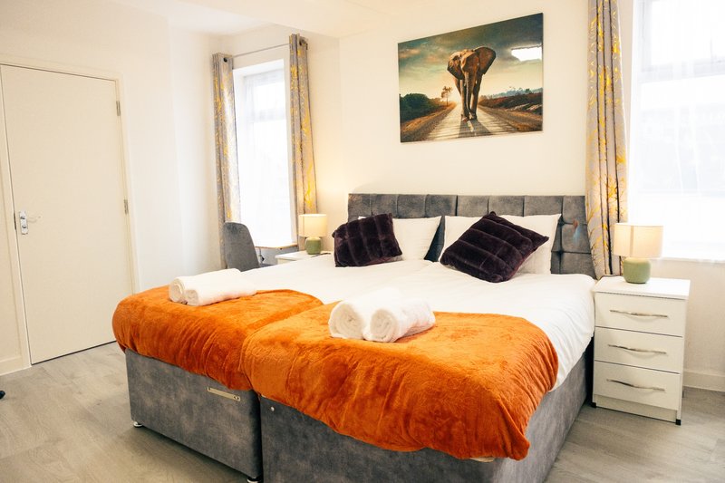 Bedroom with double bed, orange duvet, black cushions, bedside lamps and elephant wall art