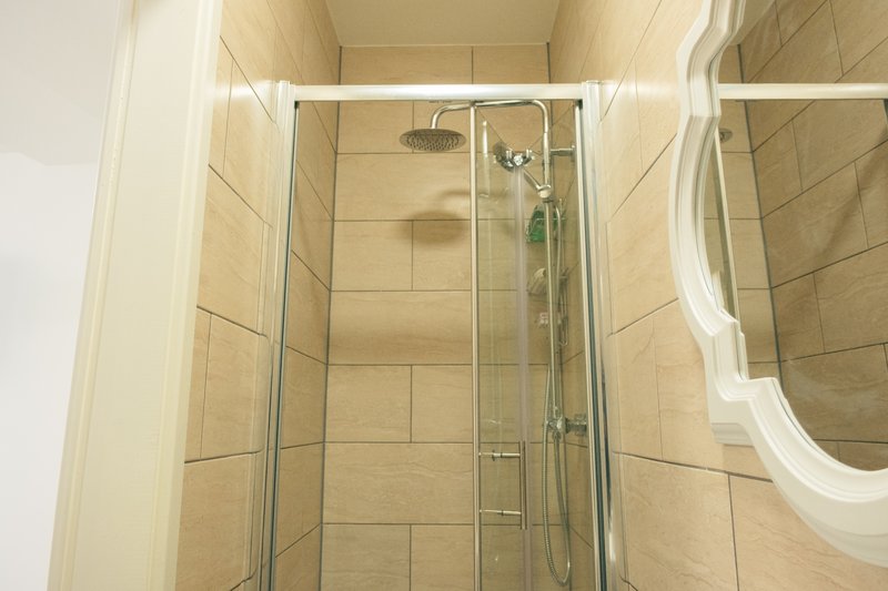 Bathroom shower enclosure with glass door, chrome fixtures and beige tile walls