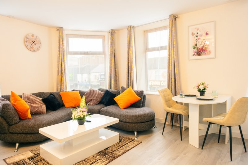Bright living room with gray corner sofa, colorful cushions, white coffee table and windows
