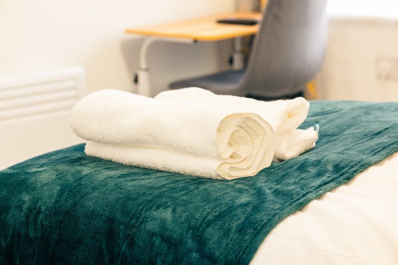 Bed with teal throw and rolled white towels arranged as decoration