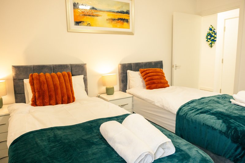 Twin bedroom with two beds, orange cushions, teal throws, white pillows and bedside lamps