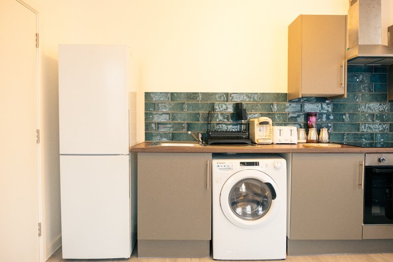 Modern kitchen with white fridge, washing machine, teal tile backsplash and wooden worktops