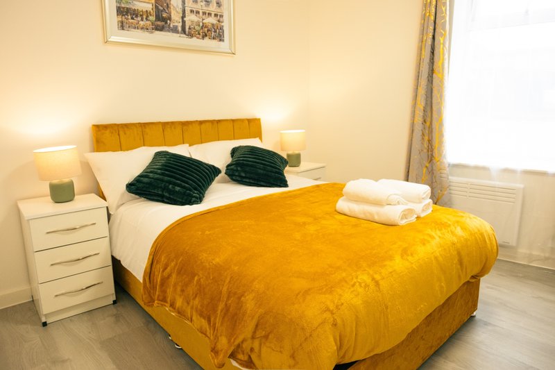 Bright bedroom with golden upholstered bed, dark pillows, white bedside tables and lamps