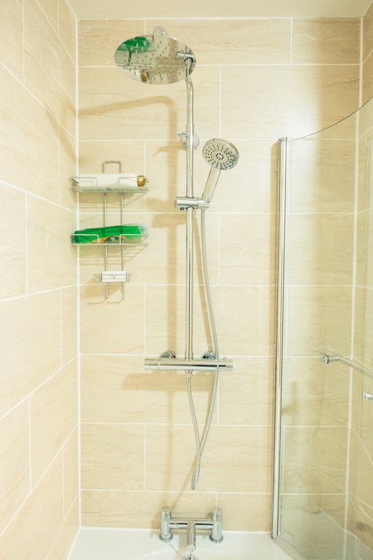 Bathroom shower cubicle with cream tiles, chrome fixtures, and green storage baskets