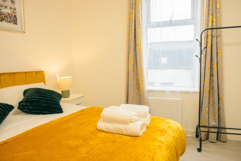 Bright bedroom with yellow bedding, green cushions, white towels and window with patterned curtains