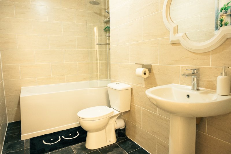 Bathroom with toilet, pedestal sink, bathtub and cream tile walls