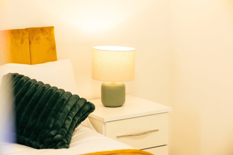 Bedroom bedside table with lamp, green cushion, and yellow headboard detail