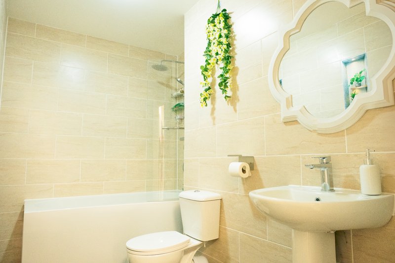 Bright bathroom with toilet, pedestal sink, bathtub, decorative mirror and hanging plant