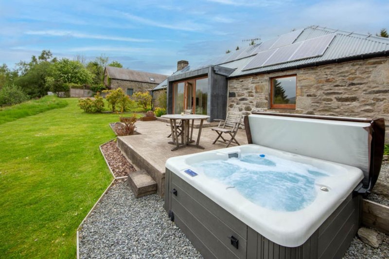 Stone cottage exterior with hot tub, patio seating, and manicured garden lawn