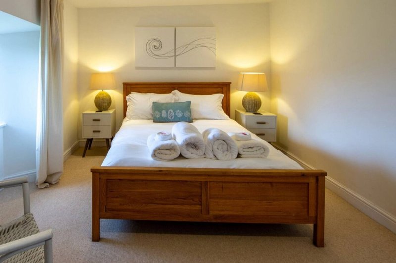 Bright bedroom with wooden bed frame, white bedding, rolled towels, and bedside lamps