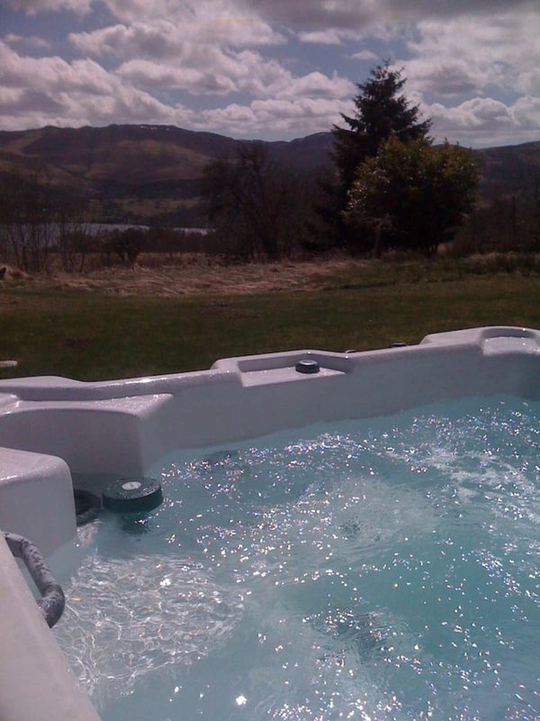 Hot tub with mountain and countryside views in background, green fields visible beyond