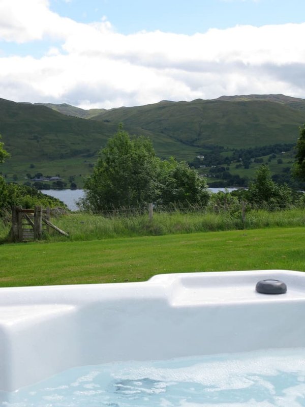 Hot tub with mountain and lake views, green lawn, trees and hills beyond