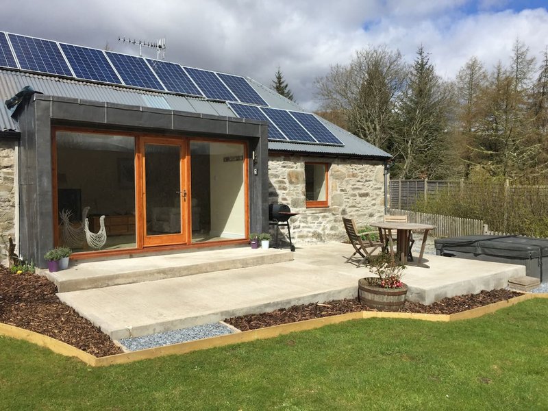 Modern stone cottage with solar panels, orange-framed glass doors, patio seating and manicured garden