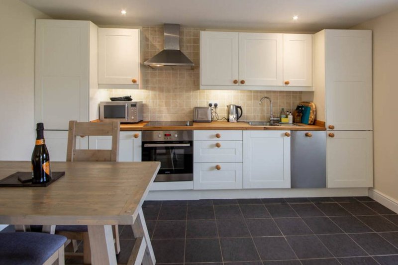 Modern kitchen with white cabinetry, wooden countertop, dining table and wine bottle
