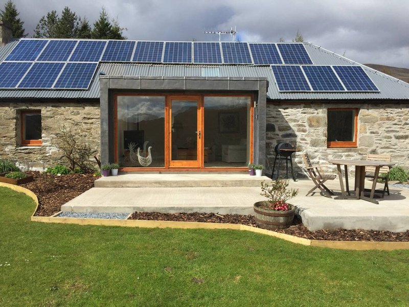 Modern stone cottage with solar panels, orange-framed glass doors, and manicured front garden