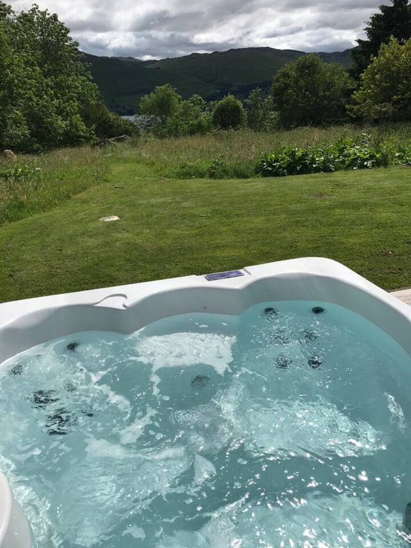 Hot tub with bubbling water overlooking garden, lawn and distant mountains