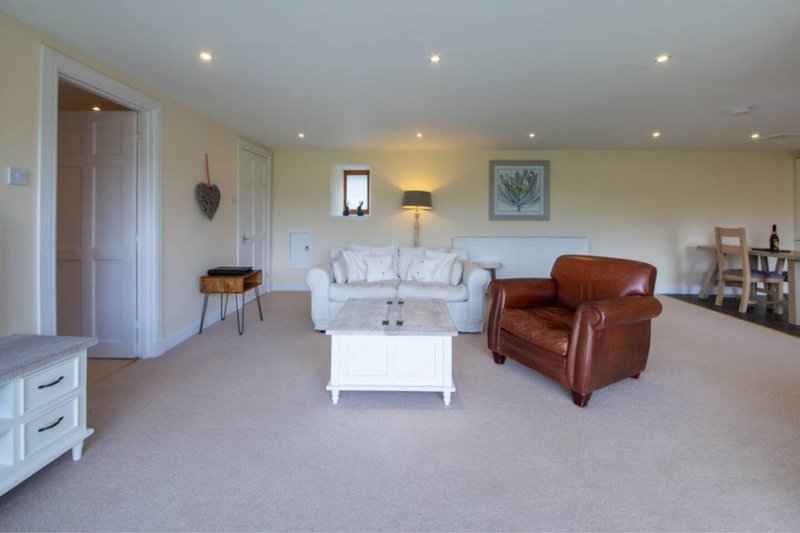 Spacious living room with cream sofa, brown leather armchair, white coffee table and recessed lighting