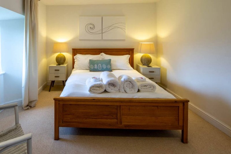 Bedroom with wooden bed frame, white bedding, rolled towels, and bedside lamps