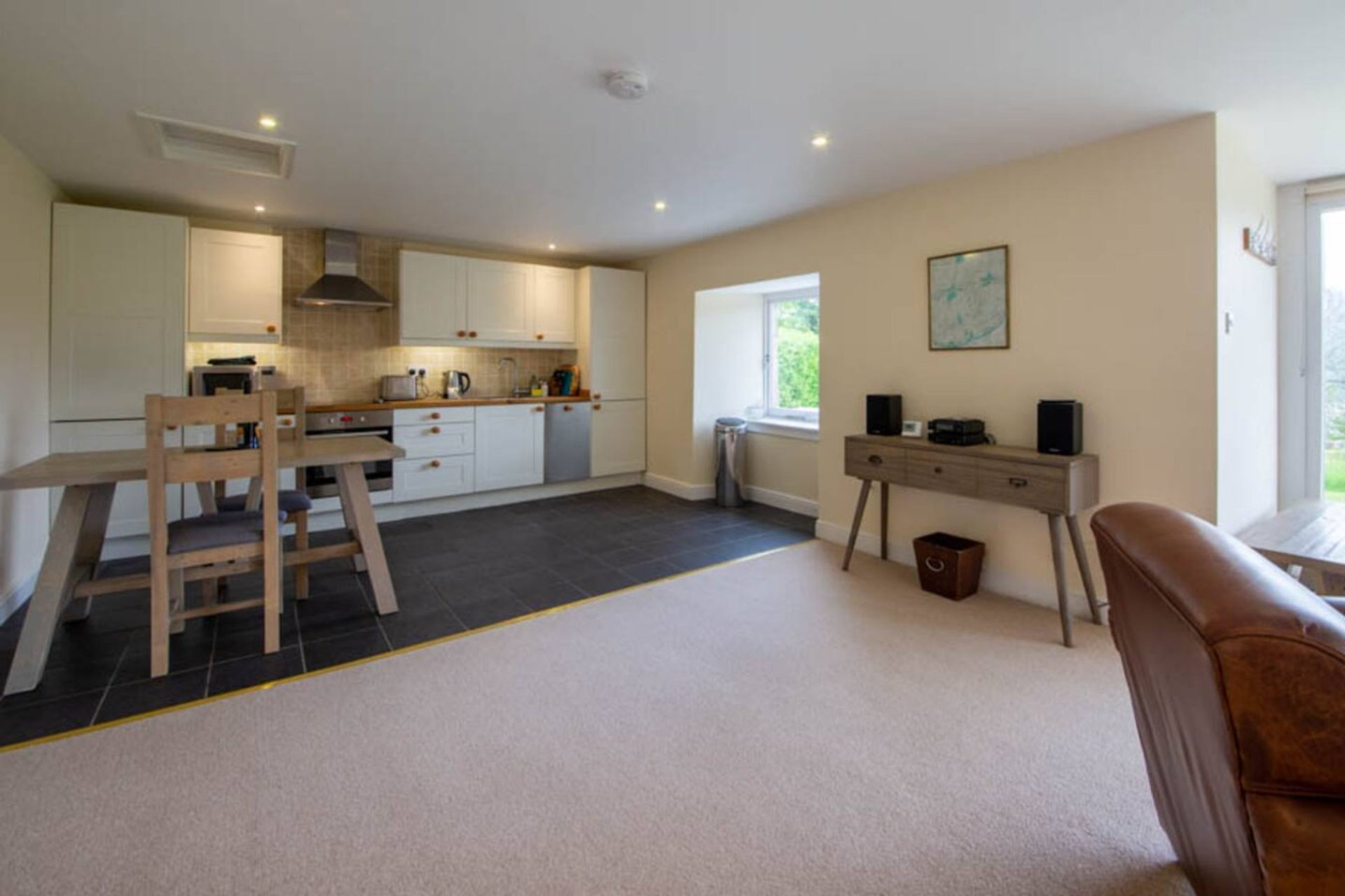 Open-plan kitchen and living area with cream cabinetry, dining table, leather sofa and garden views