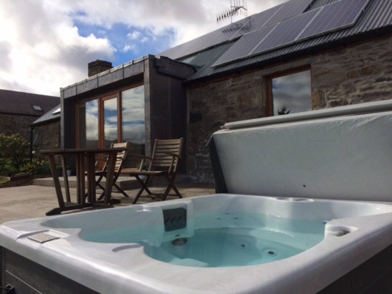 Outdoor hot tub with patio seating and stone building with dark roof